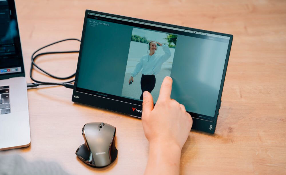 Monitor VERBATIM Light 14 cali FHD z powerbankiem 5000 mAh Czarny prezentacja monitora podczas korzystania obok laptop i myszka na biurku osoba dotykająca palcem ekran powerbank 5000mAh MagSafe bezprzewodowe zasilanie