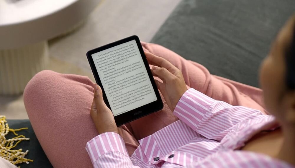 Osoba trzyma czytnik e-booków z wyświetlonym tekstem na ekranie. Osoba ubrana jest w różową piżamę w paski.