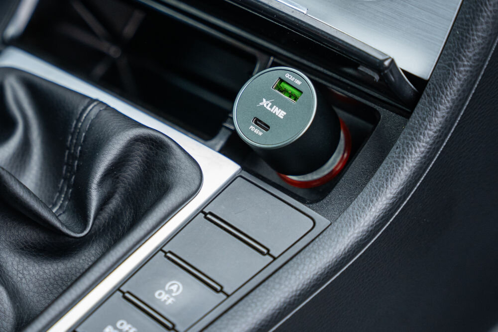 Ładowarka samochodowa w gnieździe zapalniczki z widocznymi portami USB oznaczonymi jako QC3.0 18W i PD 65W. Na ładowarce widoczne jest logo XLINE.