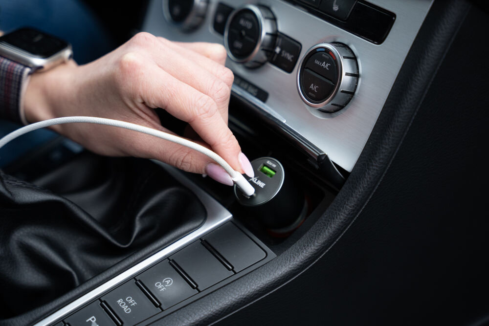 Osoba podłącza kabel do ładowarki samochodowej umieszczonej w gnieździe zapalniczki. Na ładowarce widoczny jest napis \'XLINE\'.