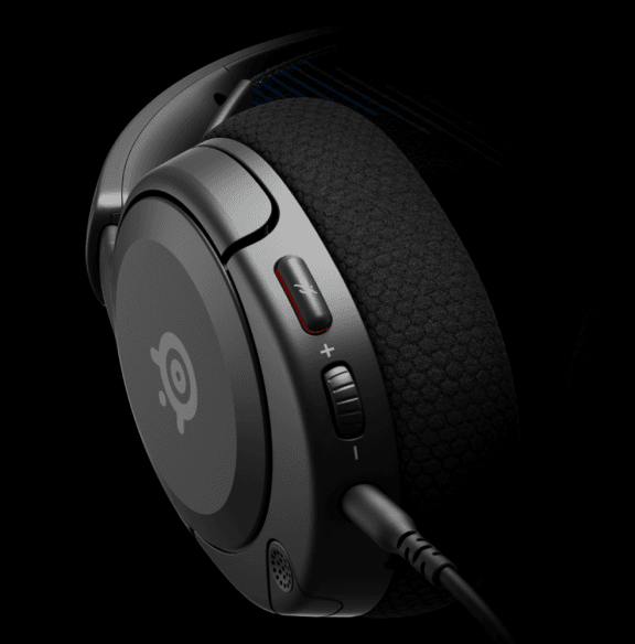 Zbliżenie na czarną nauszną słuchawkę z widocznym logo SteelSeries. Na obudowie znajdują się przyciski regulacji głośności oraz wyciszenia mikrofonu.