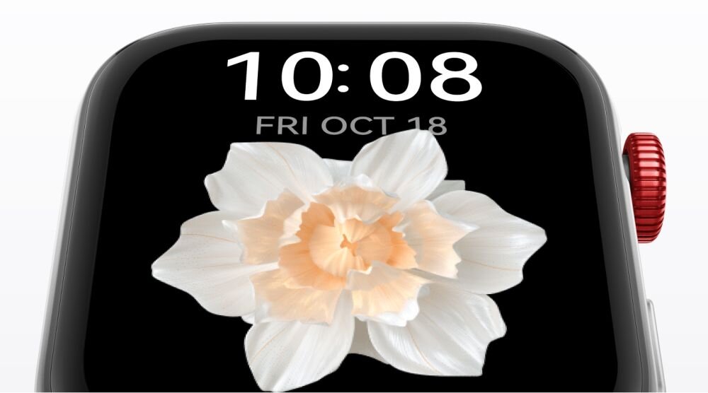 Zbliżenie na ekran smartwatcha z wyświetlaną godziną 10:08 i datą FRI OCT 18. Na tarczy zegarka widoczny jest biały kwiat z pomarańczowym środkiem.