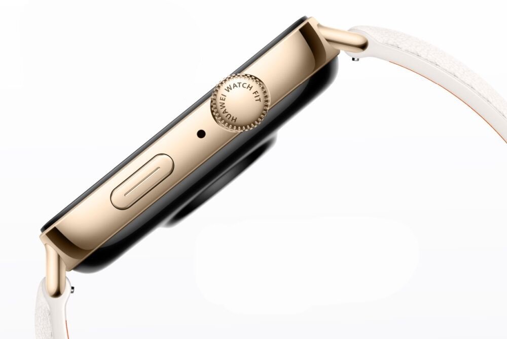 Zbliżenie na bok smartwatcha z metaliczną obudową w kolorze złotym i białym paskiem. Na pokrętle widoczny jest napis \'HUAWEI WATCH FIT\'.