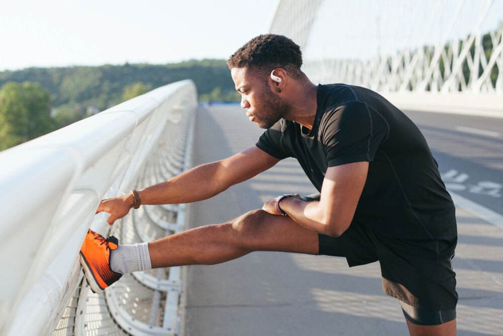 JBL Endurance Zone technologia JBL OpenSound czysty dźwięk i otwarty kanał słuchowy, osoba z założonymi słuchawkami  rozciągająca się