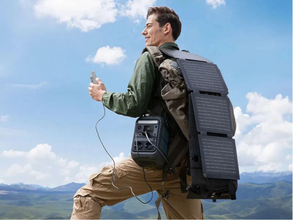 Stacja zasilania ANKER Solix C300X 288 Wh Bank energii + Panel solarny PS60 60W, ryzyko, LiFePO₄, technologia, cicho, praca, mężczyzna z pleciakiem i panelami solarnymi na nim, stoi na górzystym terenie