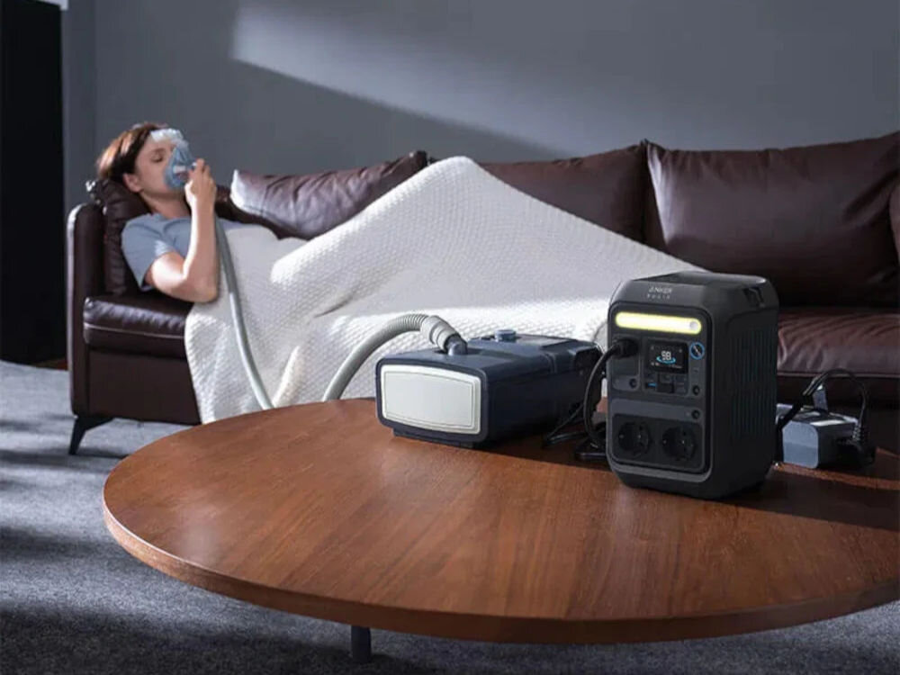 Stacja zasilania ANKER Solix C300X 288 Wh Bank energii + Panel solarny PS60 60W, elektrownia, plecak, prąd, biwak, osoba na łóżku leży chora, na pierwszym planie na stole stoi stacja zasilania