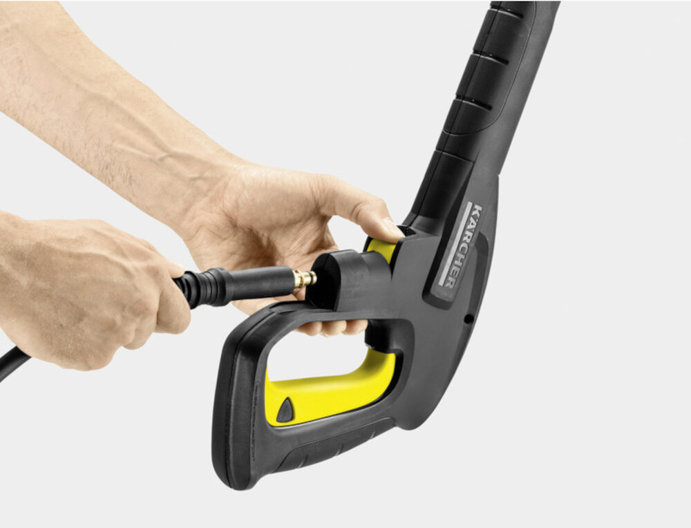 Osoba trzyma czarny pistolet ciśnieniowy z żółtymi elementami, do którego podłącza wąż. Na pistolecie widoczne jest logo \'KARCHER\'.