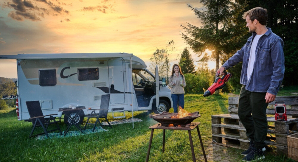 Dmuchawa do liści akumulatorowa EINHELL GE-UB 18-250 Li E Aku 4.0Ah 3433560 kamping trawa las drzewa osoba rozpala grilla w tle stoi wóz kampingowy obok wozu druga osoba 3-częściowa dmuchawa różnorodne zastosowania długa dmuchawa do liści średnia dmuchawa warsztatowa precyzyjna dmuchawa do rozpalania grilla maksymalna prędkość wylotowa na poziomie do 250 km/h