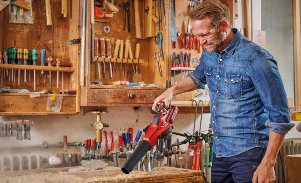 Dmuchawa do liści akumulatorowa EINHELL GE-UB 18-250 Li E Aku 4.0Ah 3433560 warsztat osoba zdmuchuje odpadki ze stołu warsztatowego w tle półki wypełnione narzędziami elektronicznej regulacji prędkości obrotowej dostosować do konkretnych potrzeb Bezproblemowe przejście od delikatnego nawiewu do intensywnego nawiewu maksymalnej wydajności nadmuchu do 120 m³/h