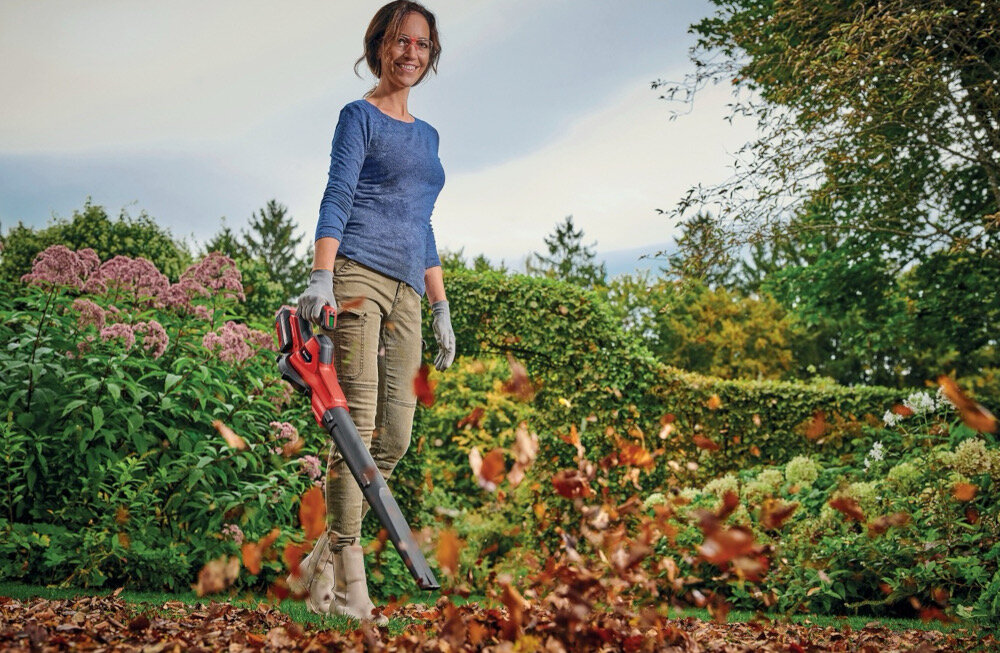Dmuchawa do liści akumulatorowa EINHELL GE-UB 18-250 Li E Aku 4.0Ah 3433560 ogród kwiaty krzewy osoba zdmuchuje liście z ziemi w tle niebo waga 3,1 kg miękka rękojeść pewny chwyt i komfort lekka konstrukcja zmniejsza zmęczenie rąk