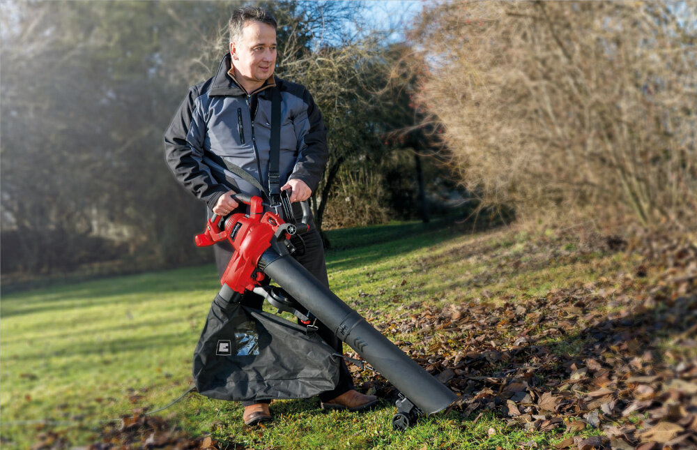 Odkurzacz do liści elektryczny EINHELL GC-EL 3000 E 3433320 ogród trawnik osoba zdmuchuje liście z trawnika w tle drzewa niebo porządek sprzątanie zasilanie elektryczne