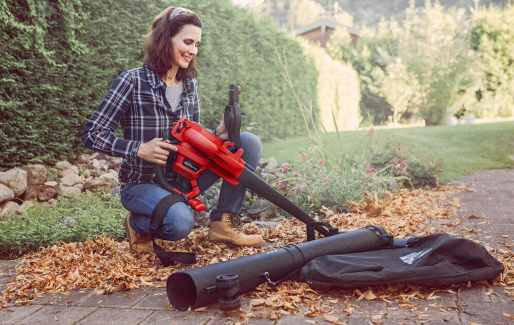 Odkurzacz do liści elektryczny EINHELL GC-EL 3000 E 3433320 ogród osoba klęczy na ziemi trzyma odkurzacz w dłoni obok leży worek na odpadki w tle trawnik drzewa niebo porządek w ogrodzie na tarasie podjeździe silnik elektryczny o mocy 3000 W stały dopływ prądu waga 5,53 kg poręczny i dobrze wyważony