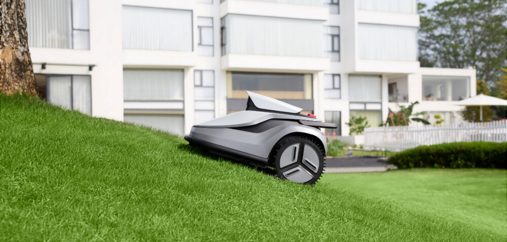 Robot koszący TERRAMOW V1000 trawnik w tle dom robot porusza się pod górkę po trawniku inteligentny system wizyjny oparty na AI porusza się samodzielnie i skutecznie bez potrzeby sygnału GPS zewnętrznych anten i ręcznego wsparcia praca na nachyleniach do 24%