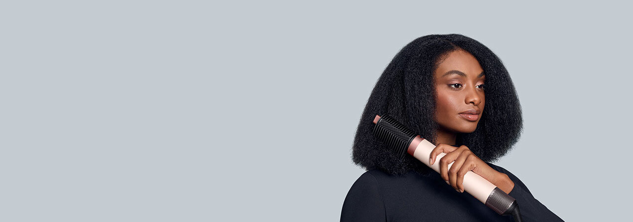 Modelka z mocno kręconymi włosami wyciąga pasma używając multistylera Dyson Airwrap Coanda2x z grzebieniem napinającym włosy.
