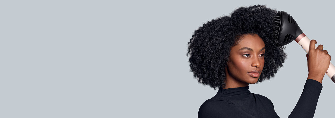 Modelka z afro stylizuje włosy przy pomocy dyfuzora używając multistylera Dyson Airwrap Coanda2x.