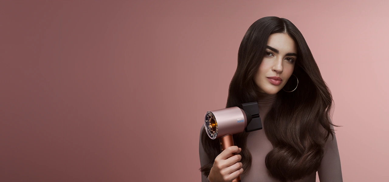 Modelka z brązowymi włosami trzyma suszarkę Dyson Supersonic Nural.