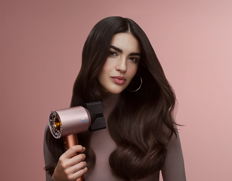 Modelka z brązowymi włosami trzyma suszarkę Dyson Supersonic Nural.
