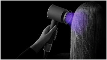 Zbliżenie na suszarkę, która emituje podświetlony na fioletowo strumień powietrza na włosy.