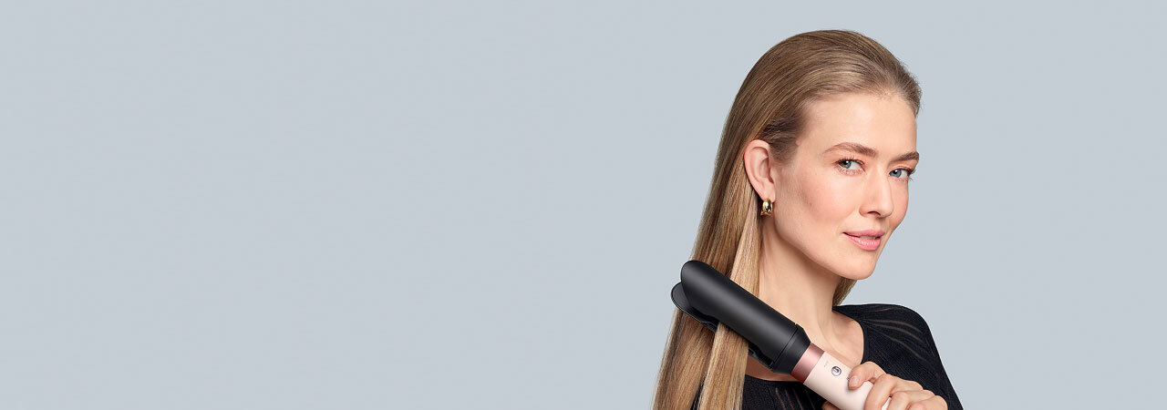 Modelka o blond włosach wygładza włosy używając multistylera Dyson Airwrap Coanda2x.