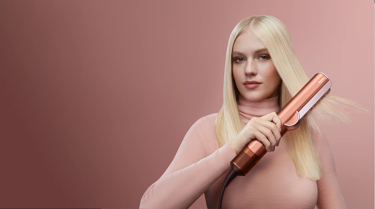 Modelka z blond włosami trzyma prostownicę Dyson Airstrait.