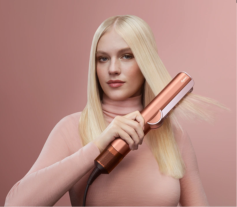 Modelka z blond włosami trzyma prostownicę Dyson Airstrait.