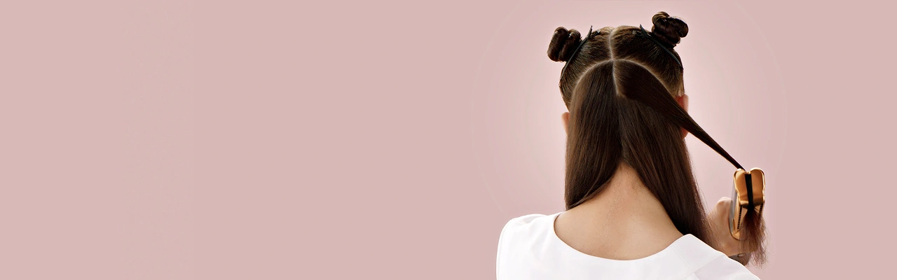 Modelk z włosami podzielonymi na sekcje widziana od tyłu podczas stylizowania pasma włosów prostownicą.