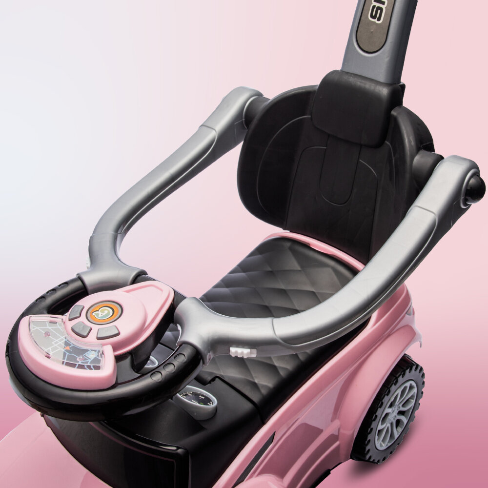 Różowy jeździk dziecięcy z czarnym, pikowanym siedziskiem i szarymi elementami. Kierownica posiada przyciski i ozdobne detale, a na rączce widoczne jest logo \'SUN\'.