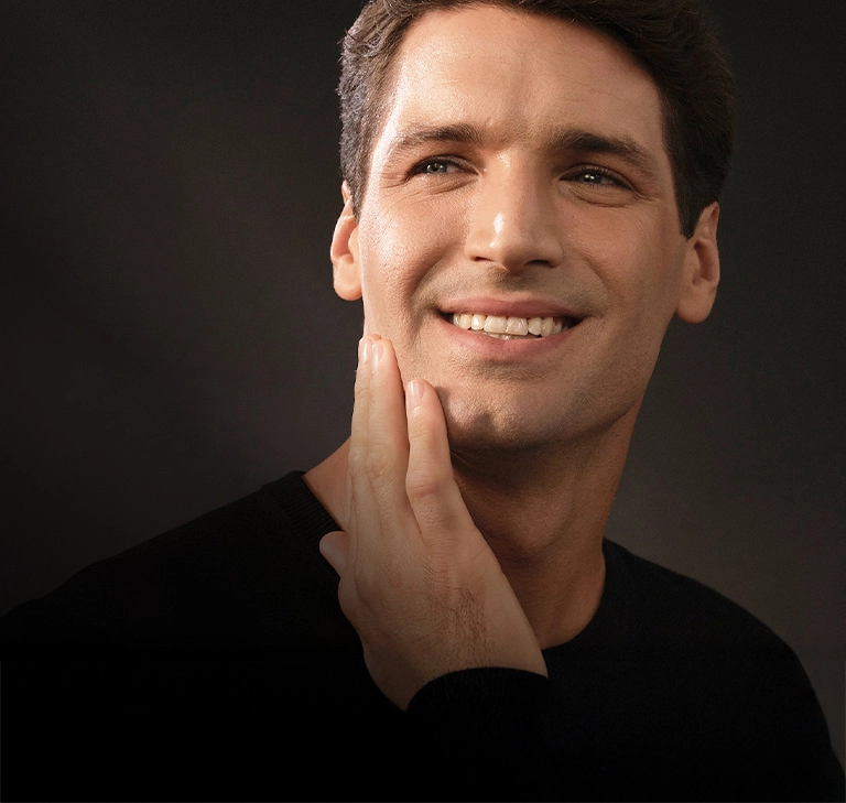 Mężczyzna uśmiecha się, trzymając rękę przy brodzie, wyrażając radość i zadowolenie.