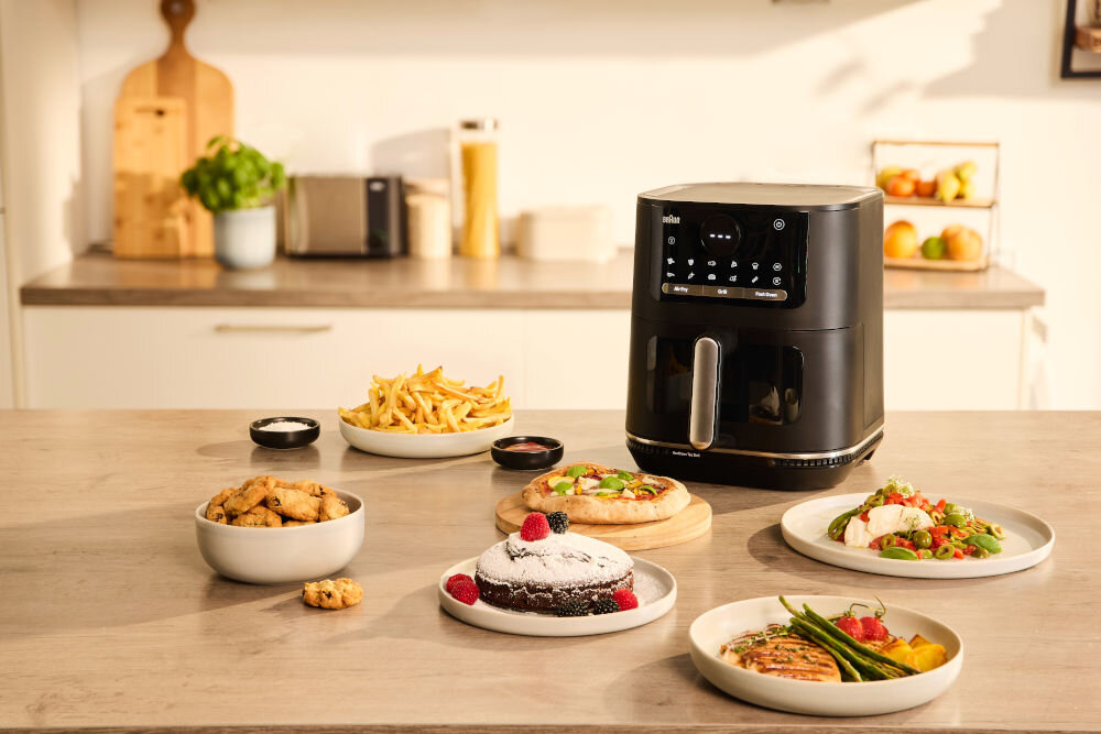 Air Fryer Frytkownica beztłuszczowa BRAUN MultiFry 5 HF5073 z 20 automatycznymi programami gotowania zdrowe gotowanie czarna frytkownica panel wyświetlacz przyciski rączka frytkownica stoi na blacie wokół potrawy na talerzach i wypieki