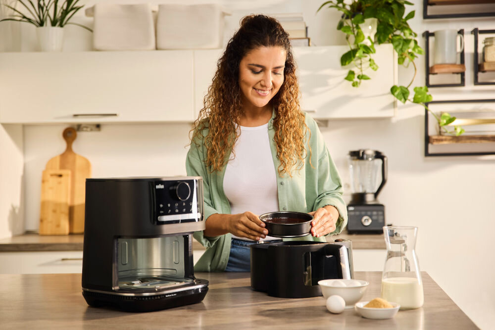 Air Fryer Frytkownica beztłuszczowa BRAUN MultiFry 5 HF5073 frytkownica stoi na blacie kobieta wkłada do kosza foremkę z ciastem z 20 automatycznymi programami gotowania zdrowe gotowanie wygoda użytkowania elektroniczny termostat dostosowanie temperatury w zakresie 80-220 stopni dopasowanie do każdej potrawy timer kontrola czasu smażenia zastosowana technologia minimalne użycie tłuszczu