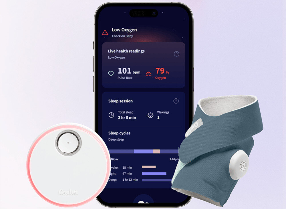 Obraz przedstawia smartfon z aplikacją monitorującą zdrowie, pokazującą niski poziom tlenu i puls 101 bpm. Obok znajduje się granatowy monitor oddechowy w formie skarpety oraz okrągłe urządzenie z logo Owlet.