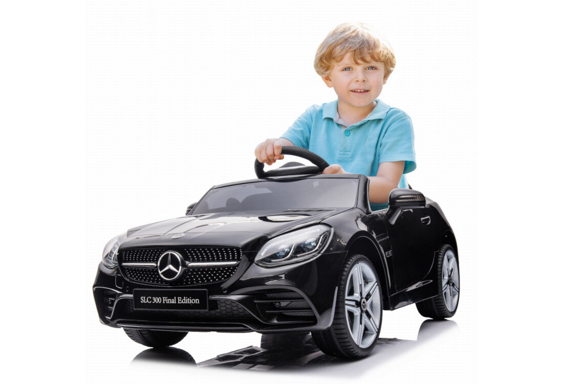 Czarny samochód dziecięcy z logo Mercedes na masce, z napisem \'SLC 300 Final Edition\' na tablicy rejestracyjnej. W samochodzie siedzi dziecko trzymające kierownicę.