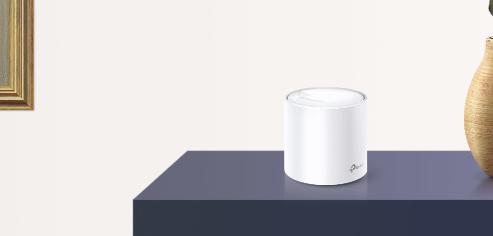 Na ciemnym blacie stoi biały, cylindryczny router z logo TP-Link. Obok znajduje się wazon, a w tle widać fragment ramki obrazu.