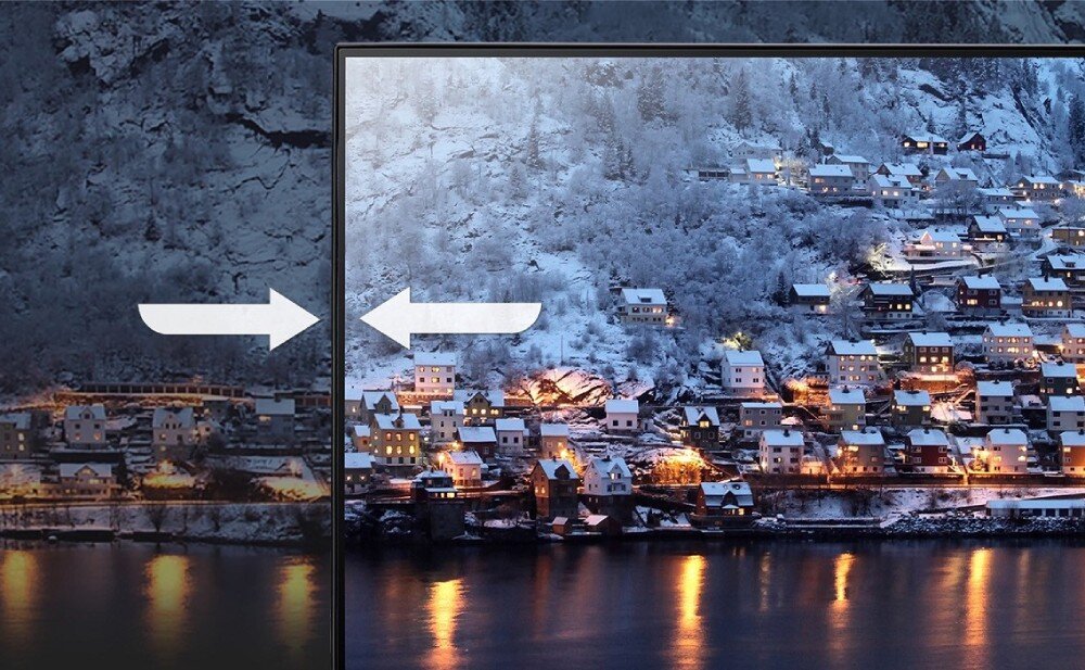 Monitor ACER SA273G0 Zbliżenie na ekran monitora, który wyświetla zimowy krajobraz z zabudowaniami. Po lewej stronie obraz jest przyciemniony, po prawej jaśniejszy i wyraźniejszy. Na środku znajdują się dwie białe strzałki wskazujące w przeciwnych kierunkach, konstrukcja, grubość, ramka