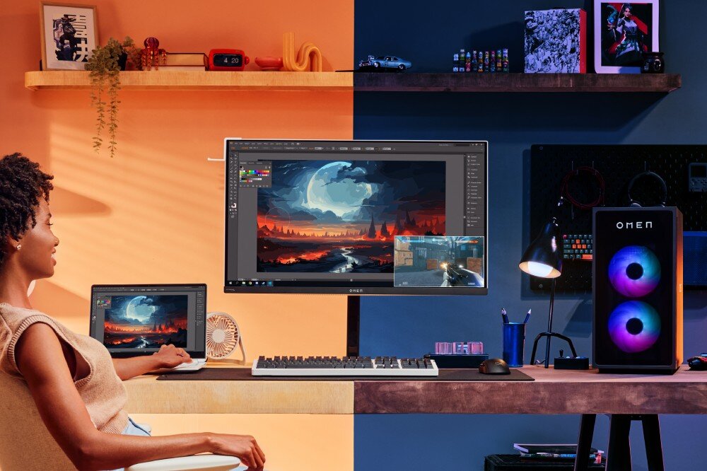 Monitor HP OMEN Transcend 9R181E9 Stanowisko komputerowe przy biurku z otwartym laptopem, podświetlaną obudową komputera oraz centralnie umieszczonym monitorem wyświetlającym grafikę i grę
