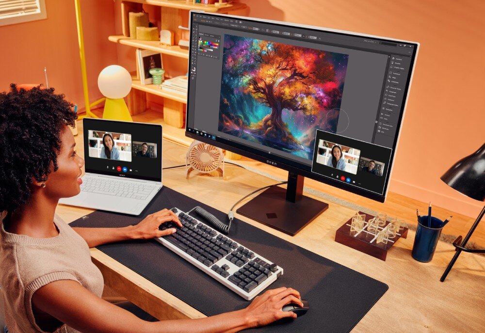 Monitor HP OMEN Transcend 9R181E9 Kobieta pisząca na klawiaturze przy biurku, na monitorze widoczny jest kolorowy obraz z drzewem oraz mniejsze okno z podglądem rozmowy wideo