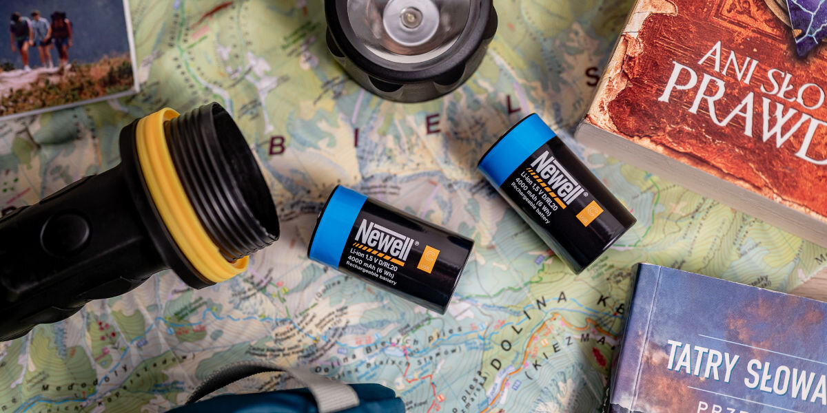 Akumulatorki NEWELL 21700 USB-C 5000 mAh (2 szt.), zestaw, akcesoria, etui, kompletność, Latarka turystyczna z dwoma włożonymi akumulatorami Newell USB-C C/R14 obok mapy Polski, książek