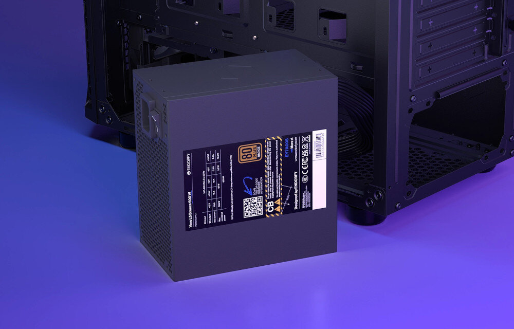 Komputer MAD DOG GeForce RTX5060 DLSS 4 Reflex Edition 2 KRUX-EXO-I07WR32WP Zasilacz komputerowy w ciemnej obudowie, z etykietą informującą o mocy i certyfikacie sprawności, umieszczony obok wnętrza komputera, zasilacz, moc, sprawność, certyfikat, zabezpieczenia