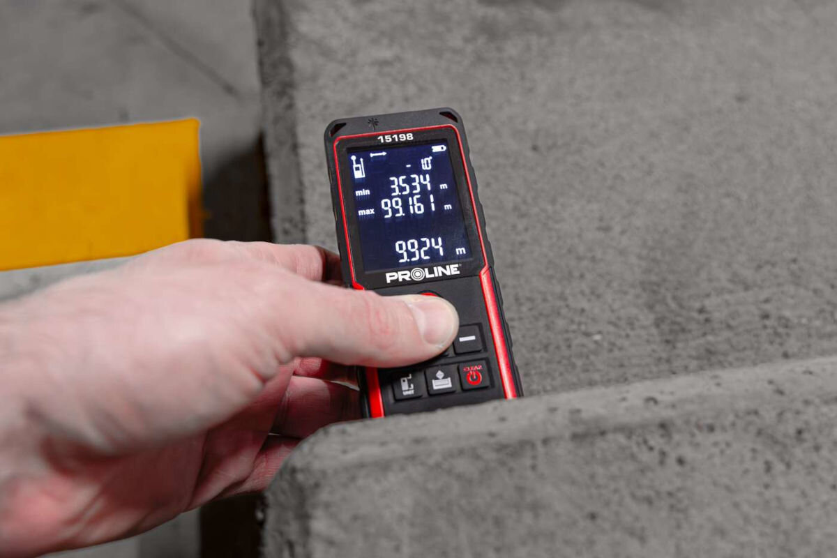 Dalmierz laserowy PROLINE 15198 70m, laser, mierzenie, odległość, dystans, dłoń trzyma dalmierz i przytrzymuje go do ścianki