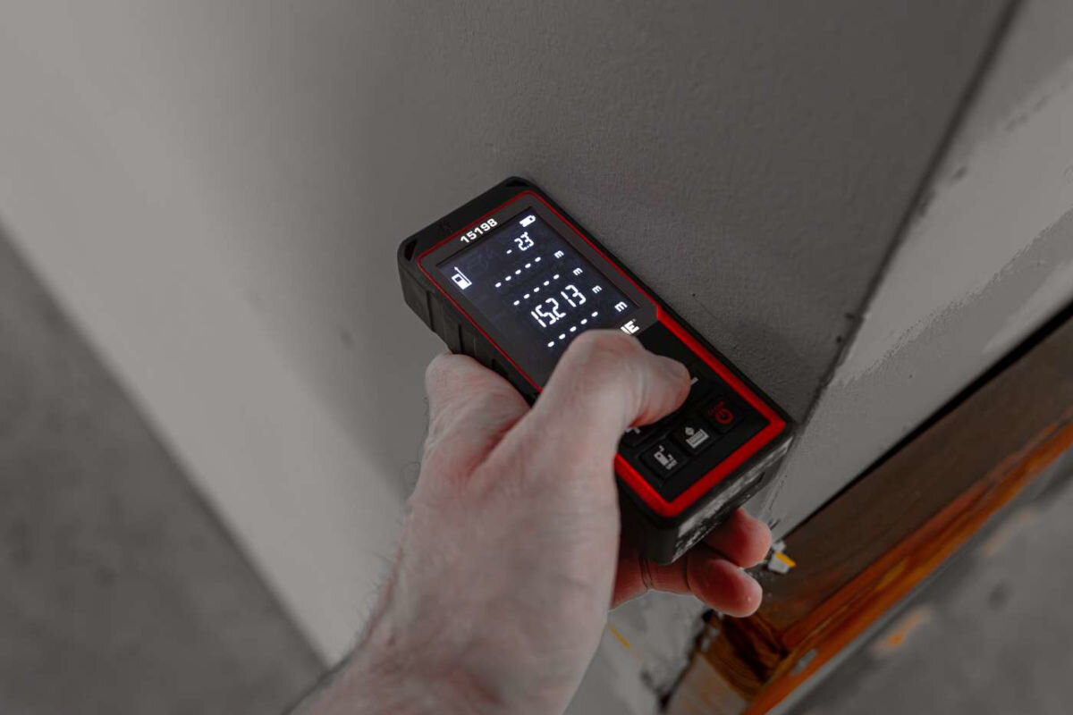 Dalmierz laserowy PROLINE 15198 70m, tryby, obliczanie, objętości, pitagoras, dłoń przytrzymuje dalmierz do ściany remontowanej