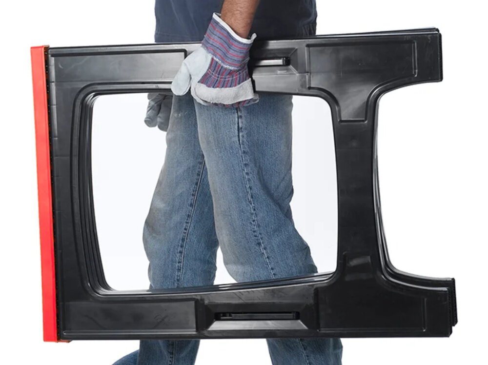 Osoba w rękawicach trzyma czarną kobyłkę warsztatową z czerwonym elementem. Widoczne są dżinsy i fragment koszuli.