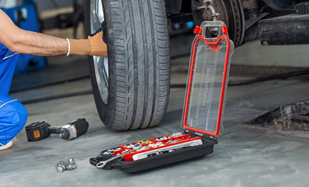 Organizer KETER 17211433 garaż warsztat otwarty organizer leży na podłodze w tle osoba zmienia koło porządek wygodne przechowywanie