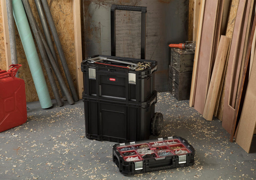 Organizer KETER Connect warsztat plac budowy organizer leży wnętrze przegródki wypełnione różnymi akcesoriami na podłodze w tle stoją dwie skrzynki porządek wygodne przechowywanie