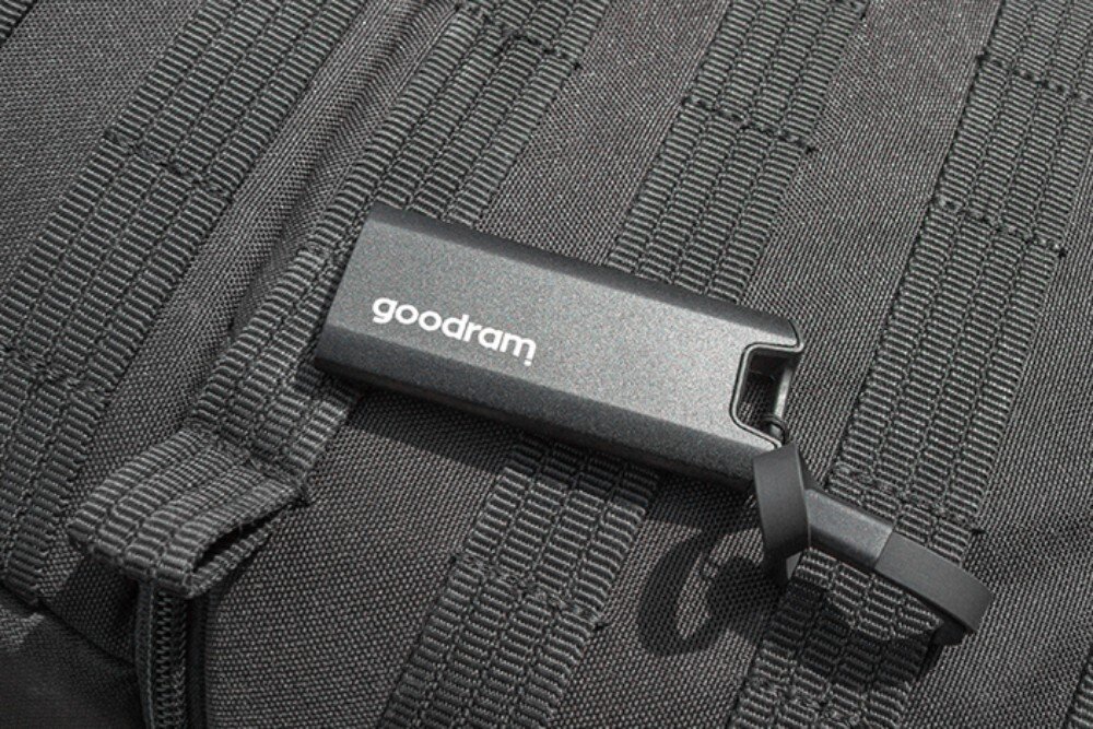 Dysk GOODRAM Move Ridge Pendrive z białym napisem 'goodram' leży na materiale plecaka z poziomymi pasami montażowymi, opis