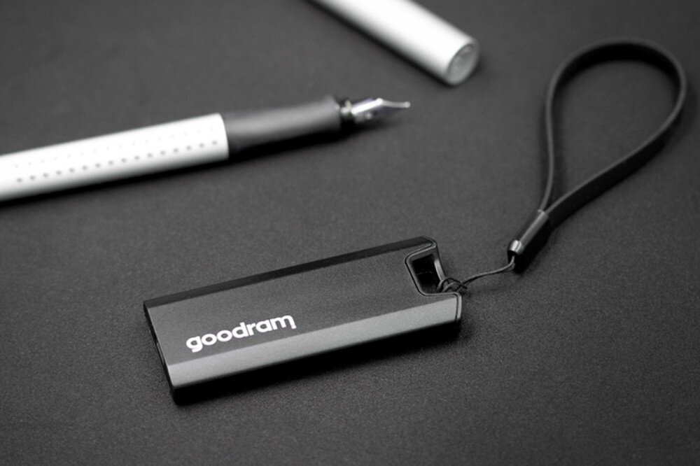 Dysk GOODRAM Move Ridge Pendrive z białym napisem 'goodram' i dołączoną smyczą leży na gładkiej powierzchni obok pióra wiecznego, wydajność, prędkość, wytrzymałość
