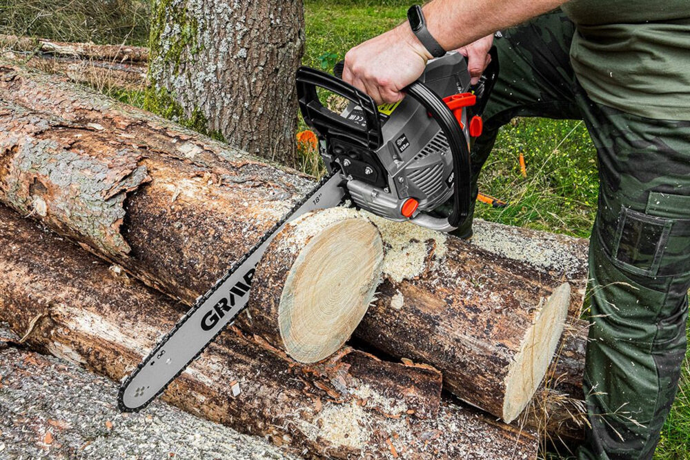 Osoba używa piły spalinowej do cięcia drewnianych kłód. Na prowadnicy piły widoczny jest napis \'GRAPHITE\'.