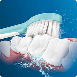 Ilustracja przedstawia szczoteczkę do zębów z turkusową rączką, która czyści białe zęby, generując białe bąbelki i wodne rozpryski na niebieskim tle.