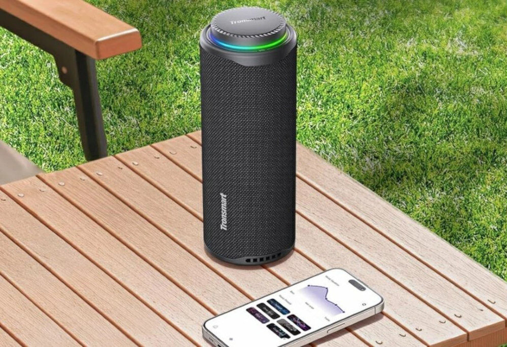 Głośnik TRONSMART T8 z aplikacją Tronsmart do EQ i trybów świetlnych, Głośnik T8 i telefon na drewnianym biurku. Na ekranie telefonu widoczny jest interfejs aplikacji Tronsmart