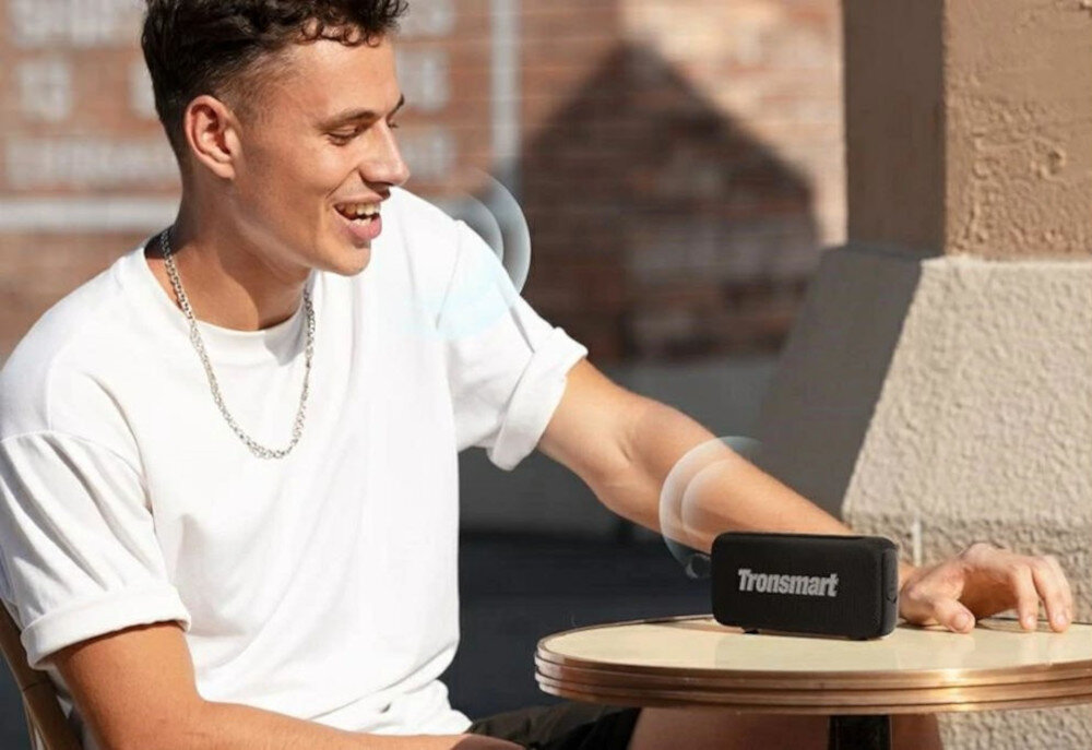 TRONSMART Trip 2 mikrofon sterowanie głosem bez użycia rąk, Mężczyzna rozmawia z głośnikiem Trip 2 stojącym na biurku na brązowym tle