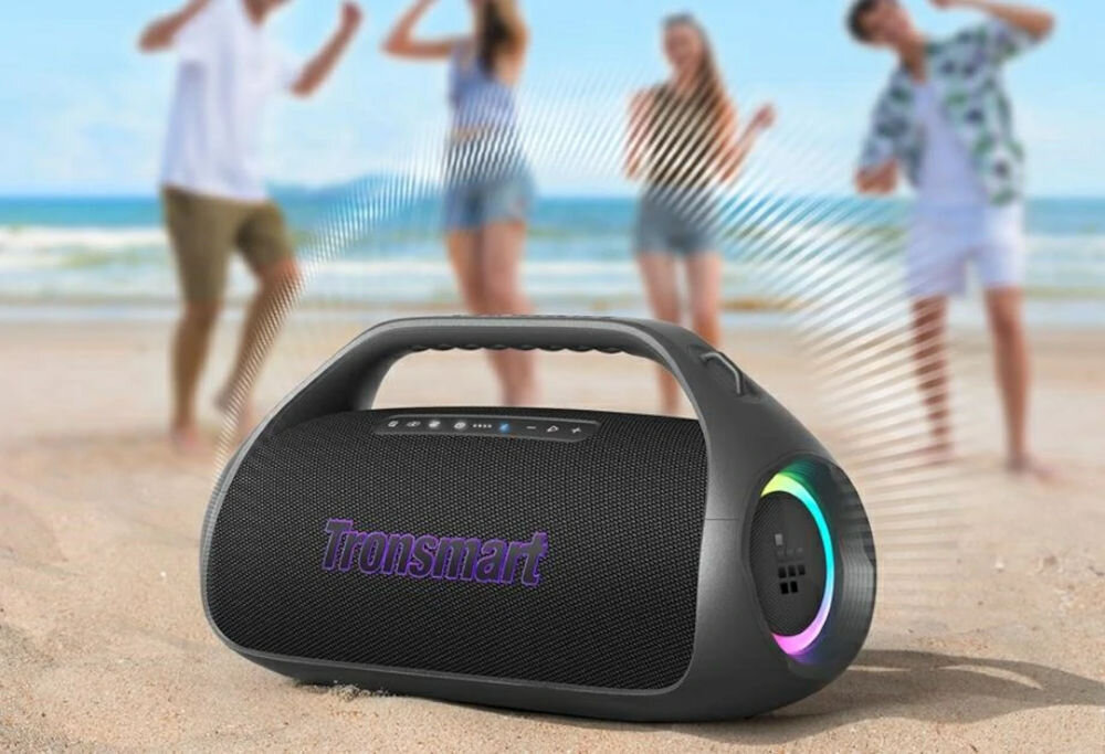 Głośnik mobilny TRONSMART Bang 2 — 90 W SoundPulse, krystaliczny dźwięk, rozległa przestrzeń, głośnik mobilny stojący na piasku nad morzem, ludzie bawiący się w rytm muzyki w tle
